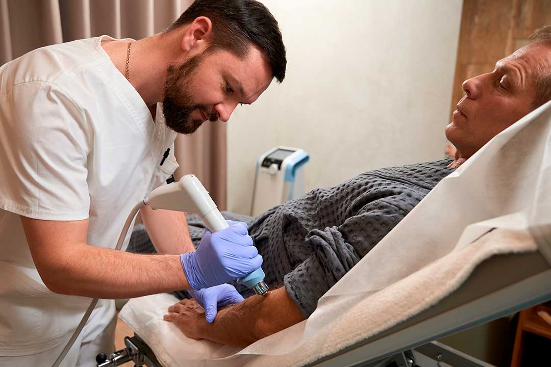 A patient in a hospital bed undergoing shockwave therapy with a healthcare professional