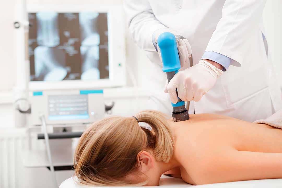 A woman undergoing shockwave therapy with a blue device, aimed at alleviating muscle tension and enhancing recovery.