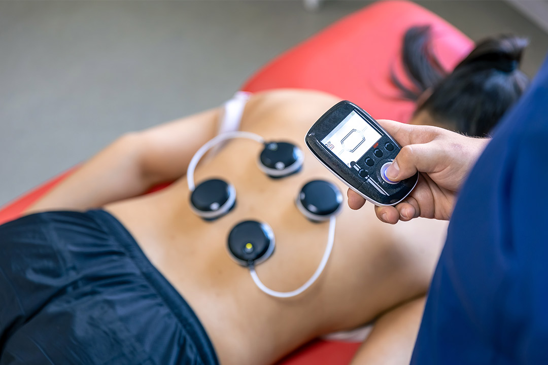 Individual receiving PEMF therapy with an electric device aimed at treating back discomfort.