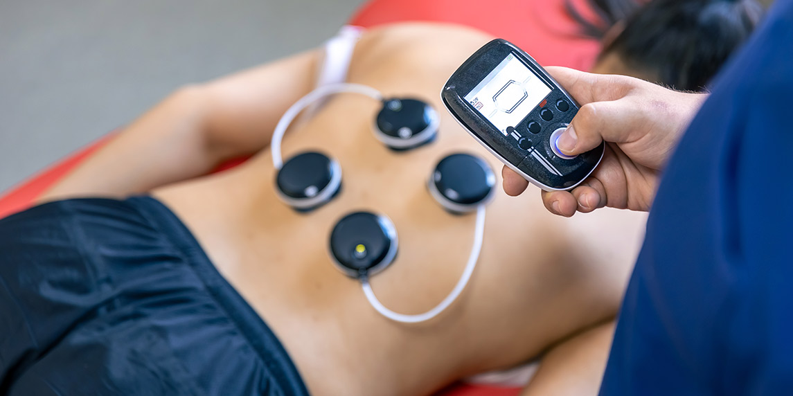  Individual applying an electric device on their back for PEMF therapy, aimed at pain relief and wellness benefits.