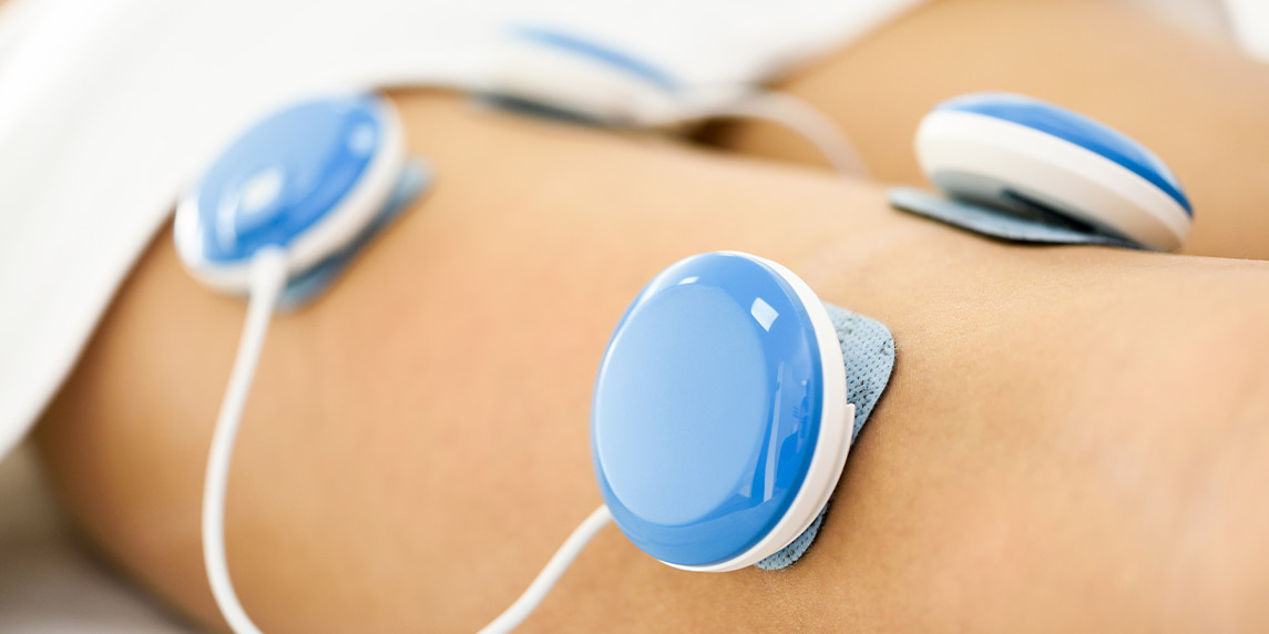  woman is using blue and white electrical devices on her abdomen, showcasing the benefits of PEMF therapy for health.